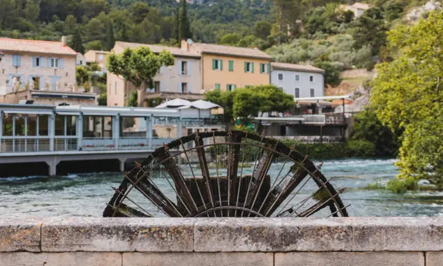Roue à aubes rouillée sur la Sorgue, avec des maisons provençales en arrière-plan. Le **gouffre de Fontaine-de-Vaucluse** est une source d'eau d'une beauté saisissante.