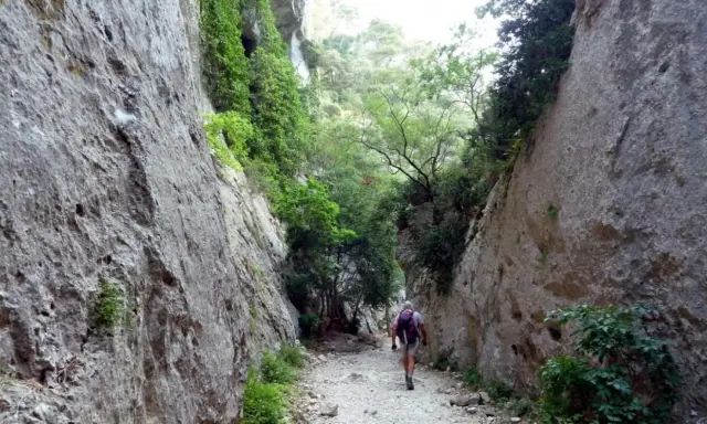 Un randonneur explore les **gorges du Régalon**, un sentier rocailleux bordé de falaises abruptes et de végétation luxuriante.