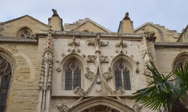 Détail architectural d'une cathédrale, un joyau du tourisme à Carpentras. Gargouilles et fenêtres gothiques sous un ciel couvert.