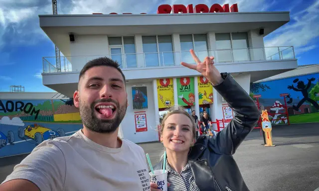 Un couple s'amuse devant le parc Spirou. La femme fait un signe de paix. Combien de temps pour faire le parc Spirou ? Une journée entière !