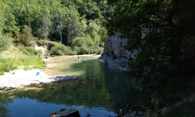 Des baigneurs profitent d'une rivière aux eaux claires près du rocher des abeilles, certains escaladent la paroi rocheuse.