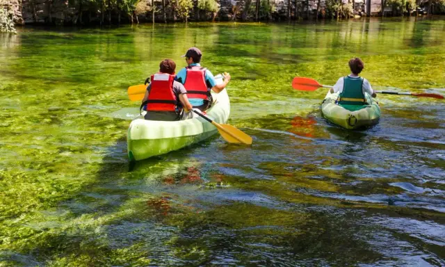 Trois personnes en canoë sur la Sorgue, profitant d'une balade paisible à L'Isle-sur-la-Sorgue. L'eau cristalline révèle la végétation sous-marine.