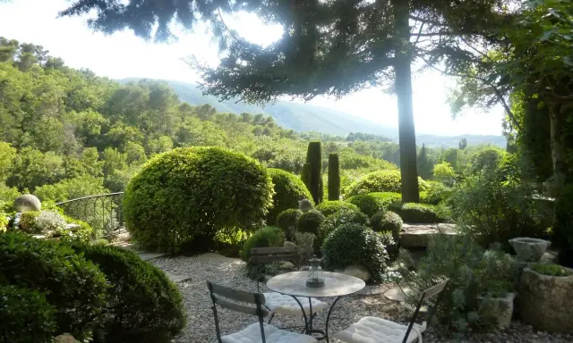 Le jardin de la louve, un havre de paix verdoyant avec une table et des chaises invitant à la détente, surplombe une vallée luxuriante.