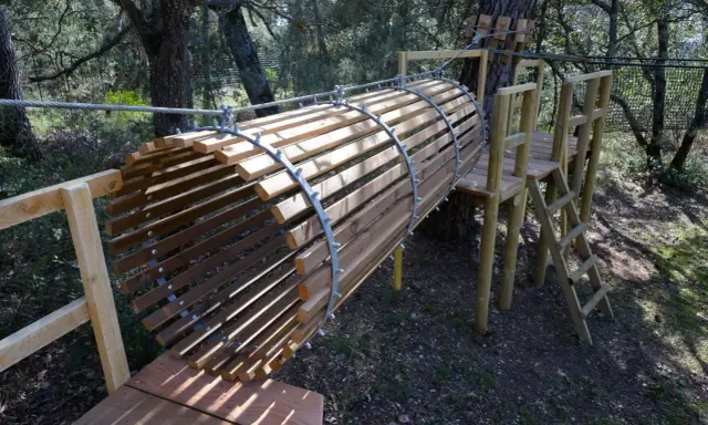 Un tunnel en bois et métal, partie d'un parcours aventure dans la forêt enchantée Venasque. Une échelle mène à une plateforme.