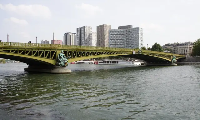 Le pont Mirabeau, avec ses statues de sirènes, enjambe la Seine, bordée par des immeubles modernes et des péniches.