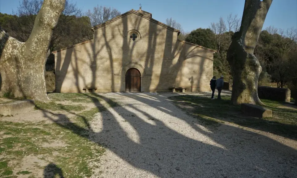 L'église de Vaugines, baignée de soleil, accueille deux visiteurs. Les ombres des arbres dansent sur sa façade de pierre.