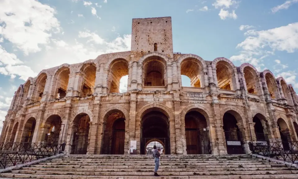 Visiter Arles : une personne tient un bébé sur les marches de l'amphithéâtre romain, sous un ciel bleu et nuageux.