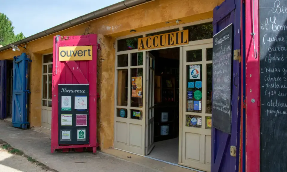 L'entrée colorée du musée des ocres, avec un panneau "Ouvert" et des affiches "Bienvenue".