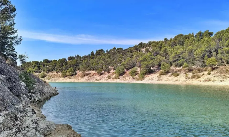 Le lac du Paty, aux eaux turquoise, est bordé de rochers et de collines verdoyantes sous un ciel bleu.