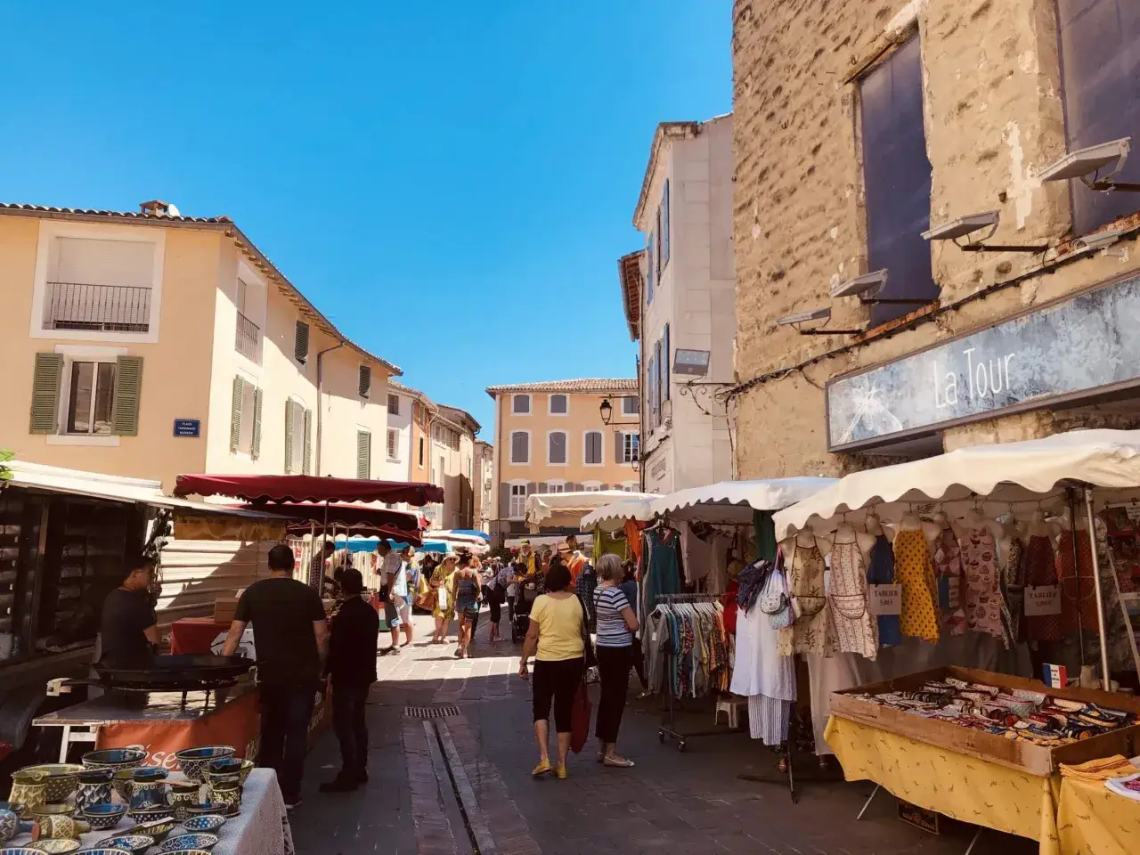 Animation des étals colorés et des passants sous le soleil éclatant du marché de l'Isle-sur-la-Sorgue.
