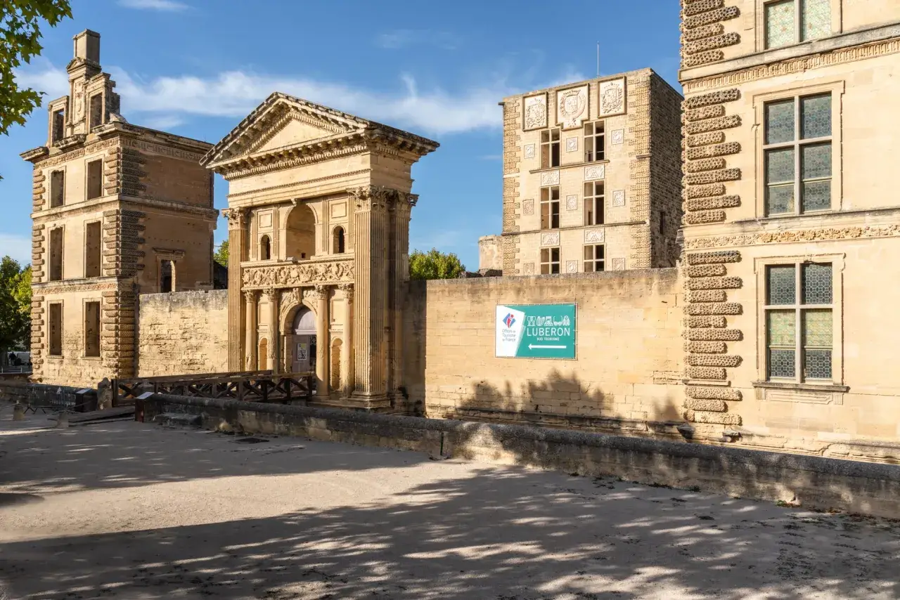 La Tour d'Aigues, un château Renaissance en Provence, se dresse sous un ciel bleu. Une passerelle en bois mène à son entrée ornée.
