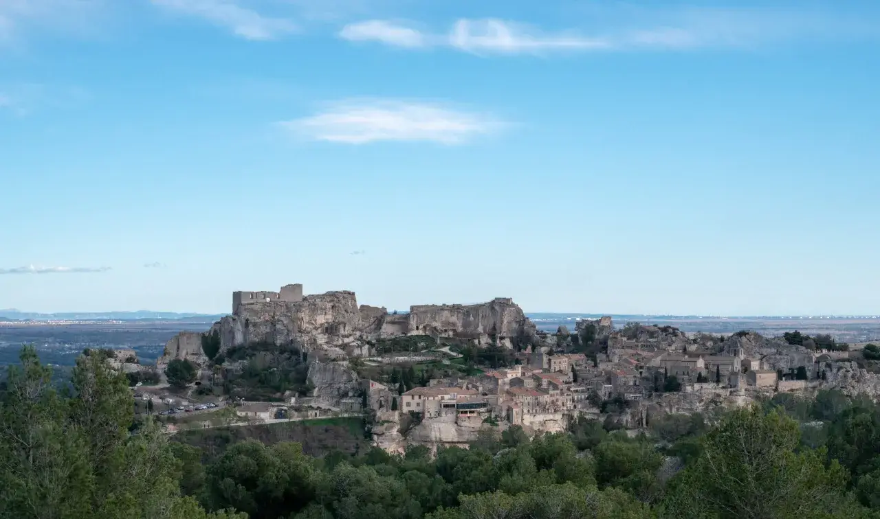 Vue panoramique du village perché des Baux-de-Provence, avec son château médiéval en ruines dominant les maisons de pierre et la végétation verdoyante.
