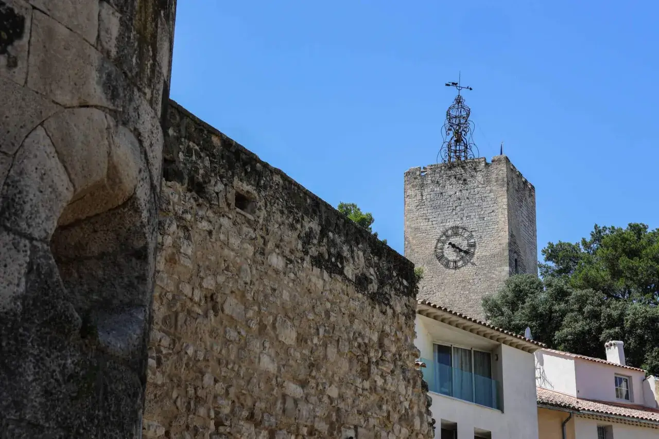 Vieille tour de l'horloge à Pernes-les-Fontaines, avec un mur de pierre ancien au premier plan.