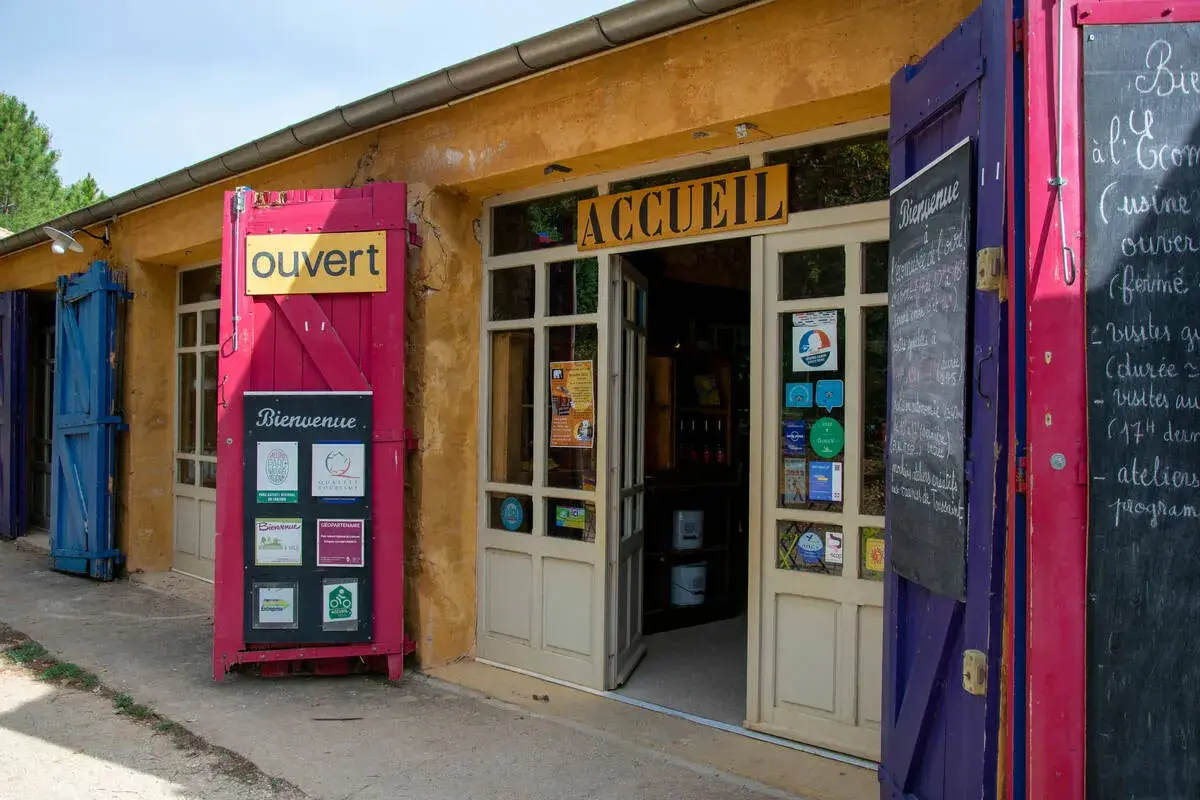 L'entrée colorée du musée des ocres, avec un panneau "Ouvert" et des affiches "Bienvenue".