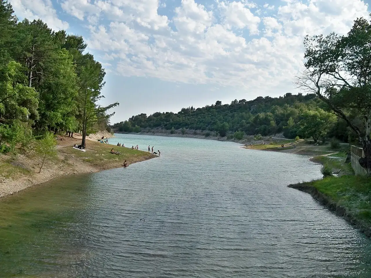 Journ&eacute;e ensoleill&eacute;e au lac du Paty, o&ugrave; des baigneurs profitent de l'eau turquoise et des rives ombrag&eacute;es par les pins.