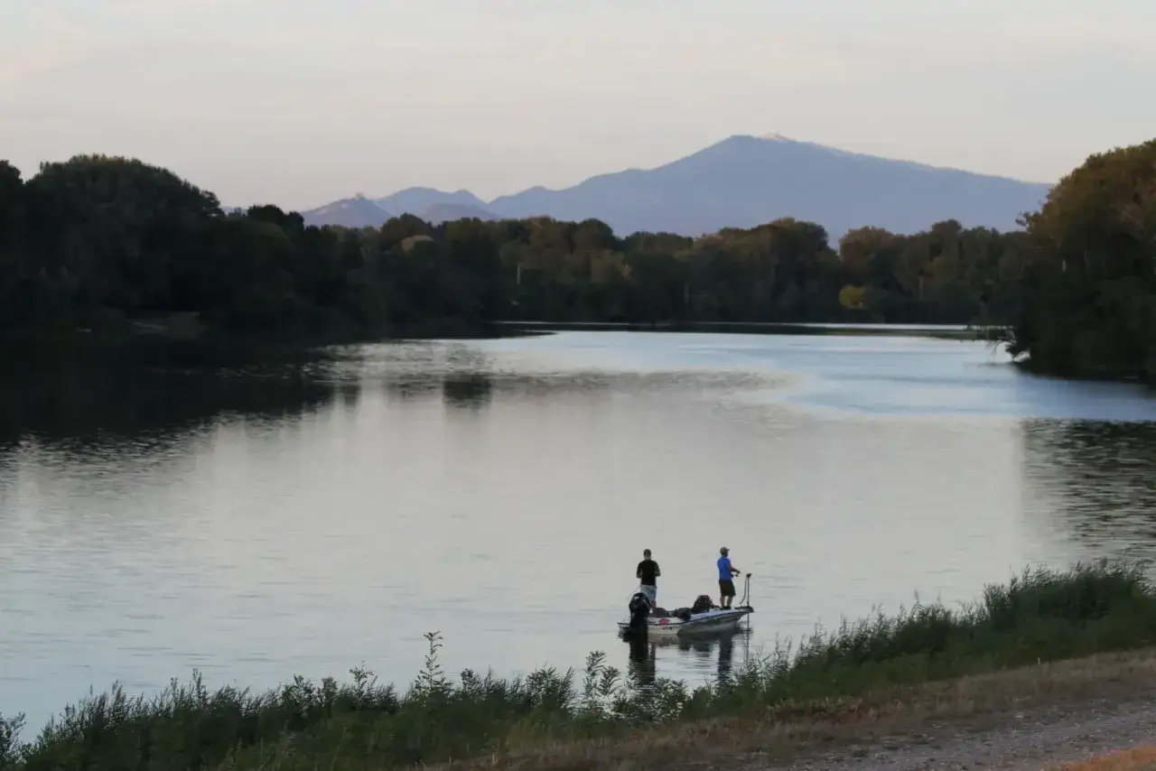 Deux p&ecirc;cheurs sur un bateau profitent du calme du plan d'eau du Revestidou, avec des montagnes en arri&egrave;re-plan.