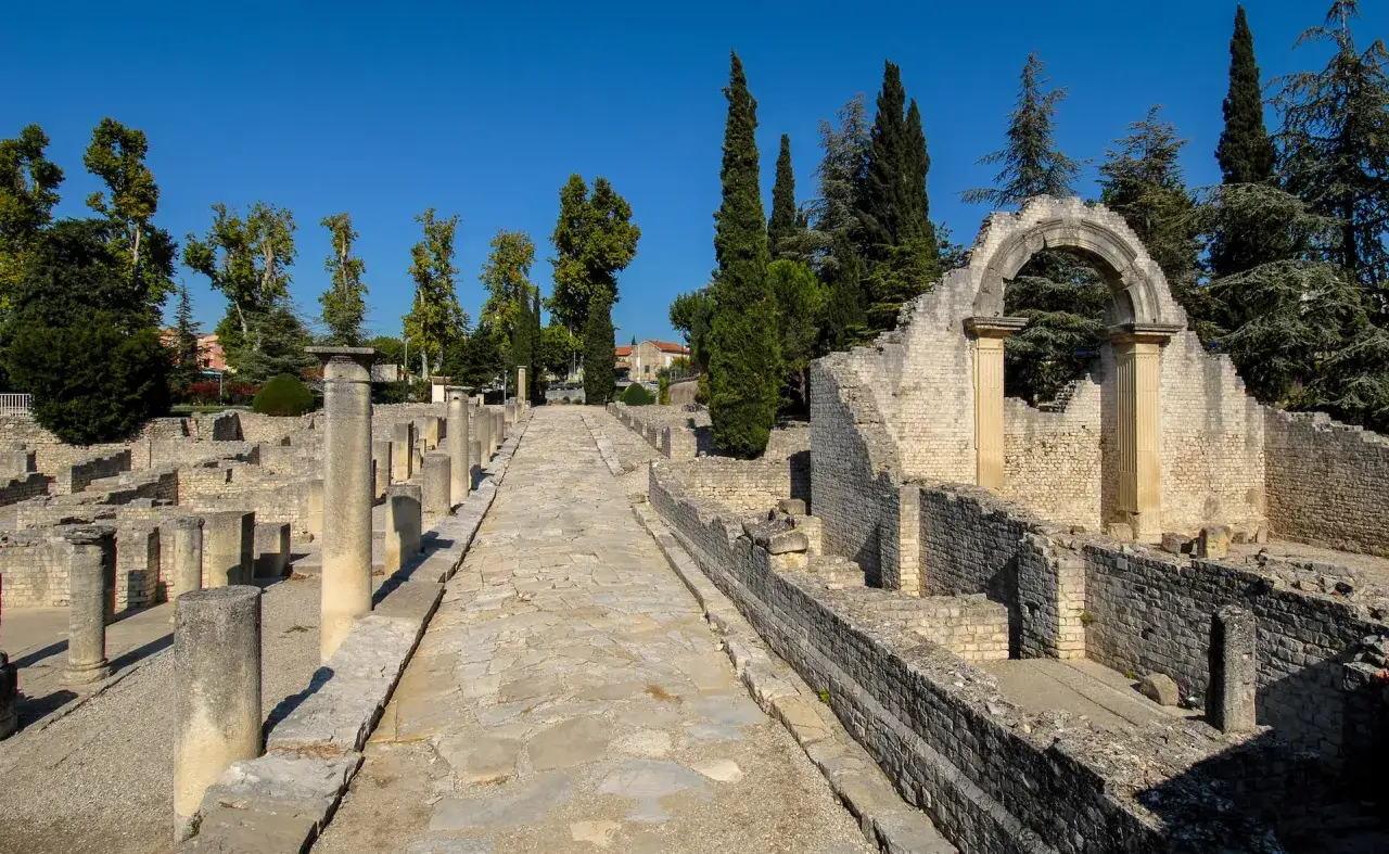 Vestiges romains &agrave; Vaison-la-Romaine : une all&eacute;e pav&eacute;e m&egrave;ne &agrave; travers des ruines de colonnes et de murs de pierre sous un ciel bleu.