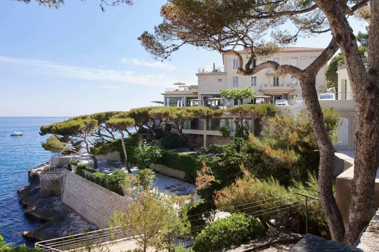 Un hôtel de luxe en bord de mer, avec des pins tortueux rappelant un cheval blanc en Provence, surplombant la Méditerranée.