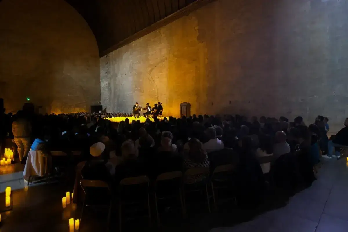 Concert aux chandelles dans un lieu historique pour une expo avignon. Musiciens sur scène, public assis dans la pénombre.