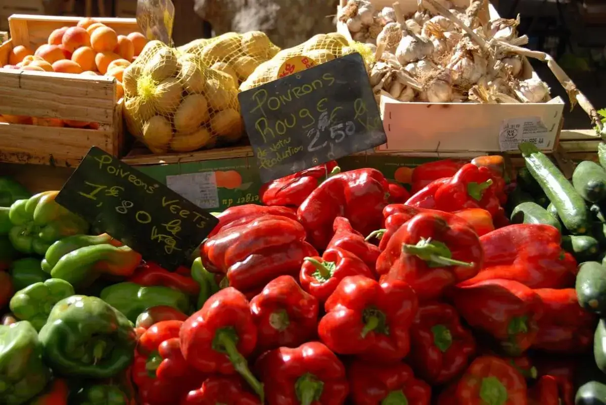 Poivrons rouges et verts vifs au march&eacute; de Cavaillon, avec des abricots, des pommes de terre et de l'ail en arri&egrave;re-plan.