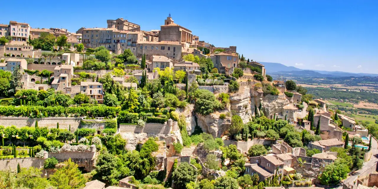 Village perché de Gordes, avec ses maisons en pierre et ses jardins luxuriants, évoquant l'ambiance d'un marché provençal animé.