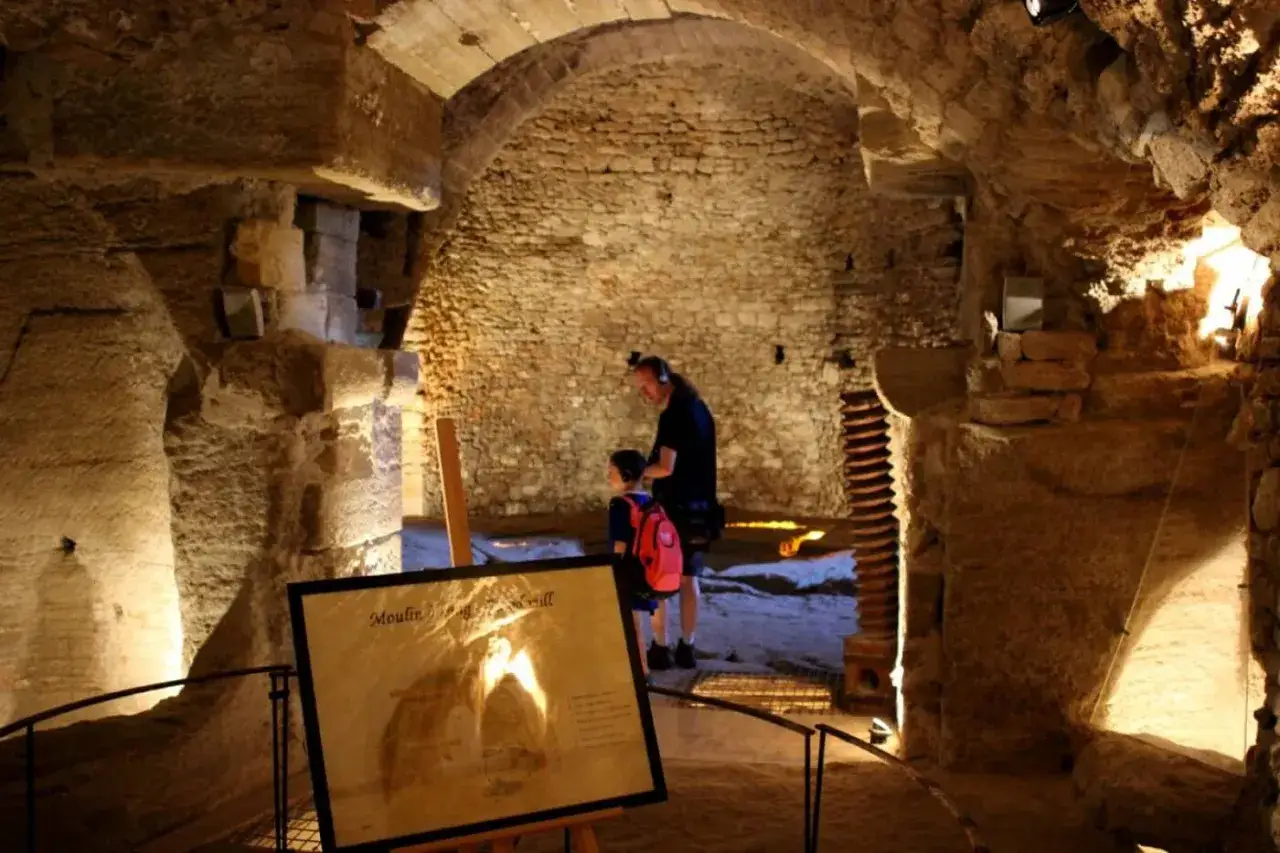Un homme et un enfant explorent les caves du palais saint-firmin, un lieu historique aux vo&ucirc;tes de pierre.