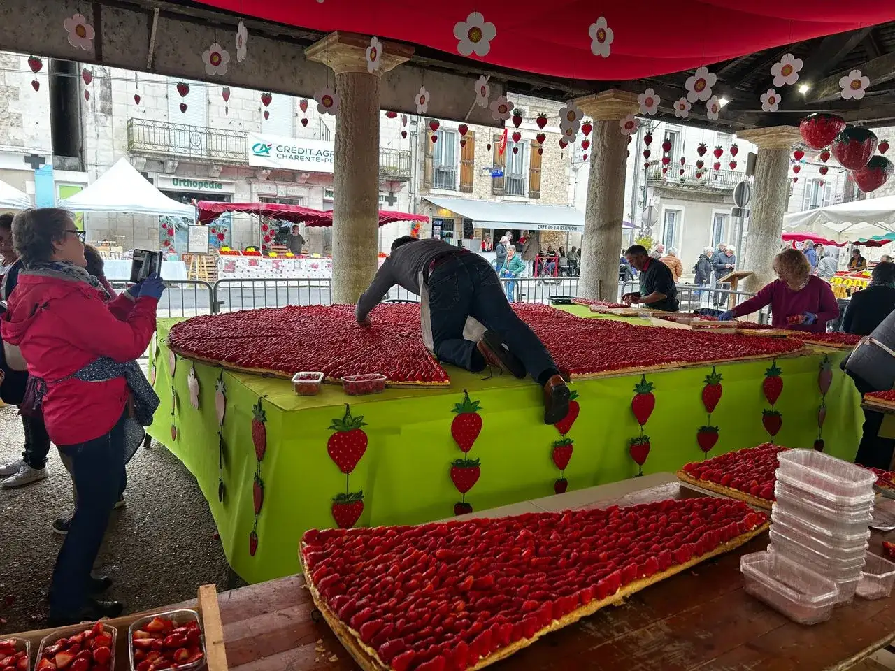 Une immense tarte aux fraises est pr&eacute;par&eacute;e pour la f&ecirc;te de la fraise. Des d&eacute;corations de fraises et de fleurs ornent l'espace.