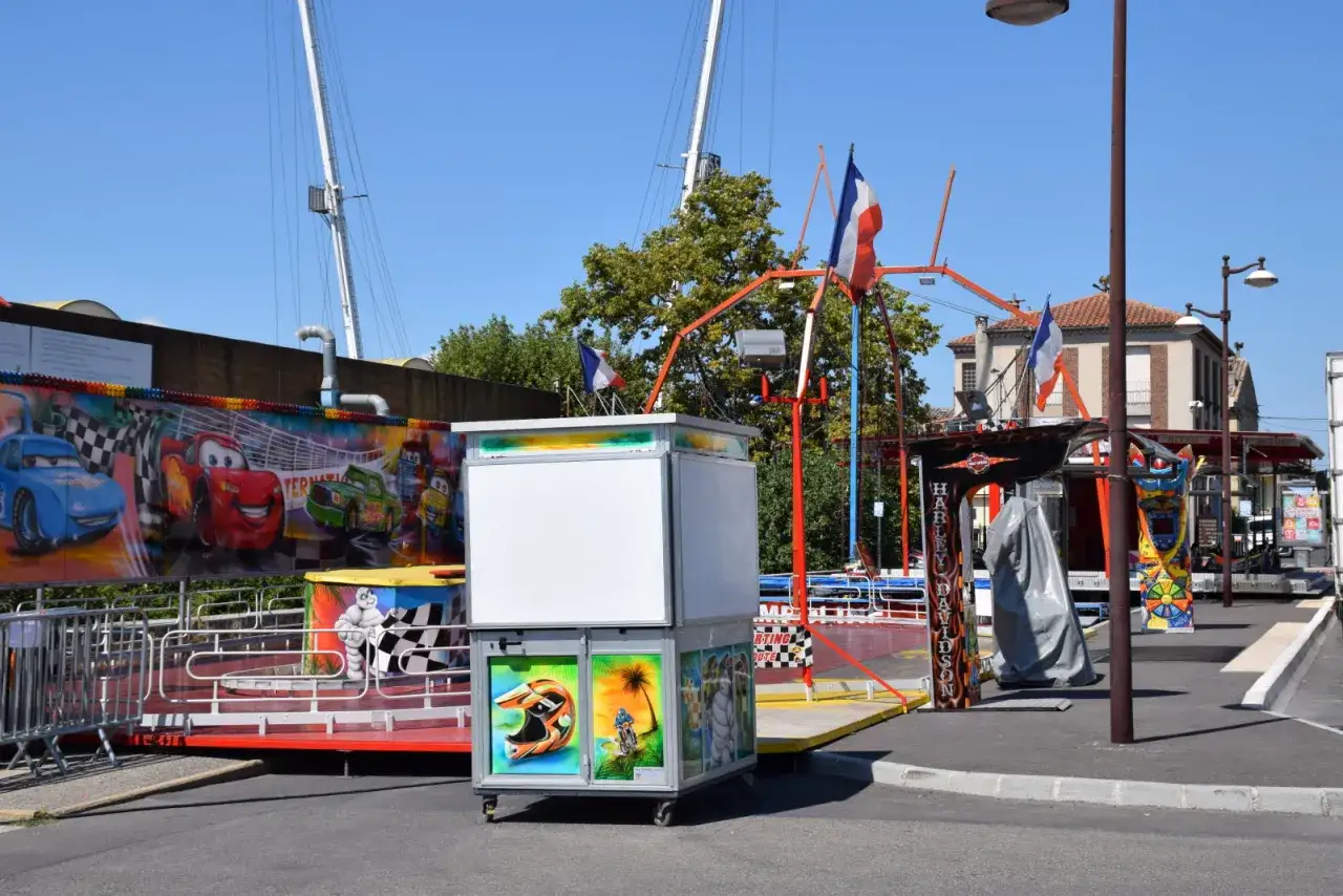 Attractions de la fête foraine à L'Isle-sur-la-Sorgue, avec des décorations de voitures de course et des drapeaux français.