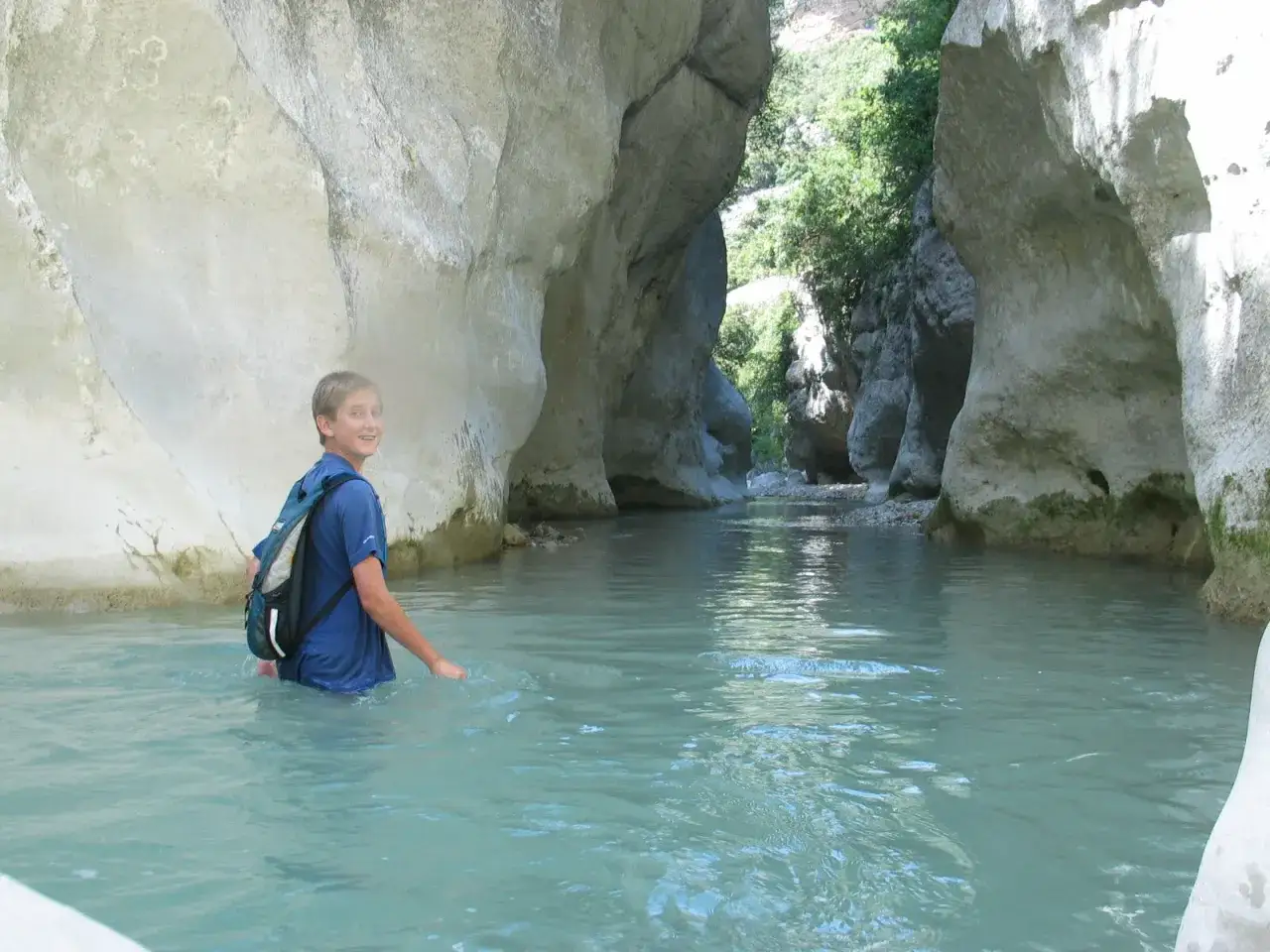 Un jeune gar&ccedil;on avec un sac &agrave; dos explore la gorge du Toulourenc, marchant dans l'eau turquoise entre les falaises calcaires.