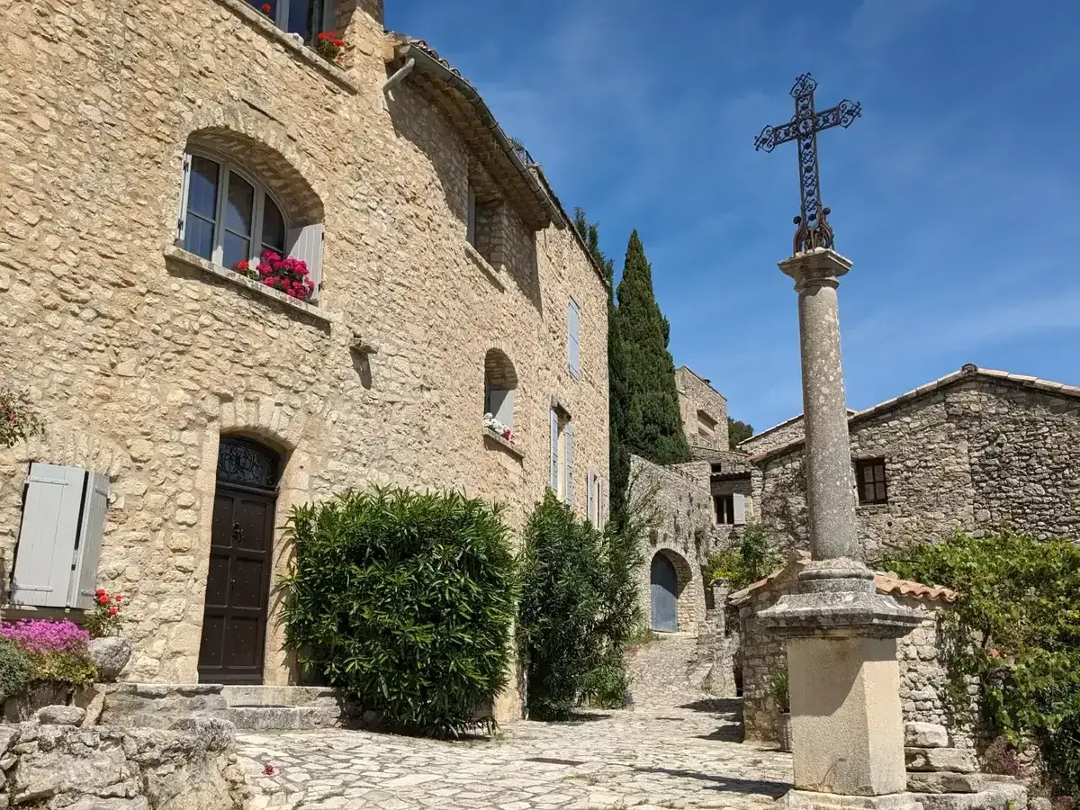 Village de pierre au soleil, le Crestet Vaucluse, avec sa croix monumentale et ses maisons fleuries.