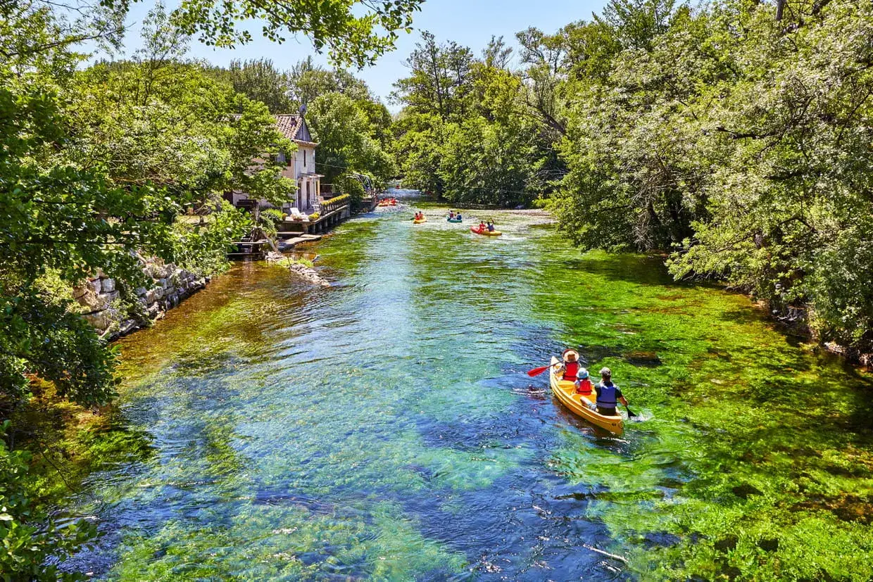 Une famille en cano&euml; profite de la Sorgue &agrave; L'Isle-sur-la-Sorgue, entour&eacute;e de verdure luxuriante et d'eau cristalline.