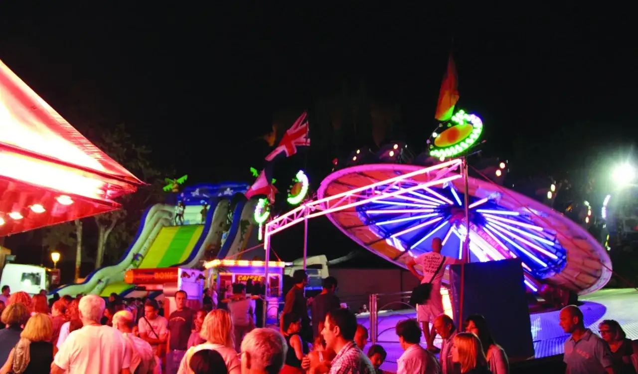 Ambiance de fête foraine 84, attractions lumineuses, toboggan gonflable et foule animée sous le ciel nocturne.