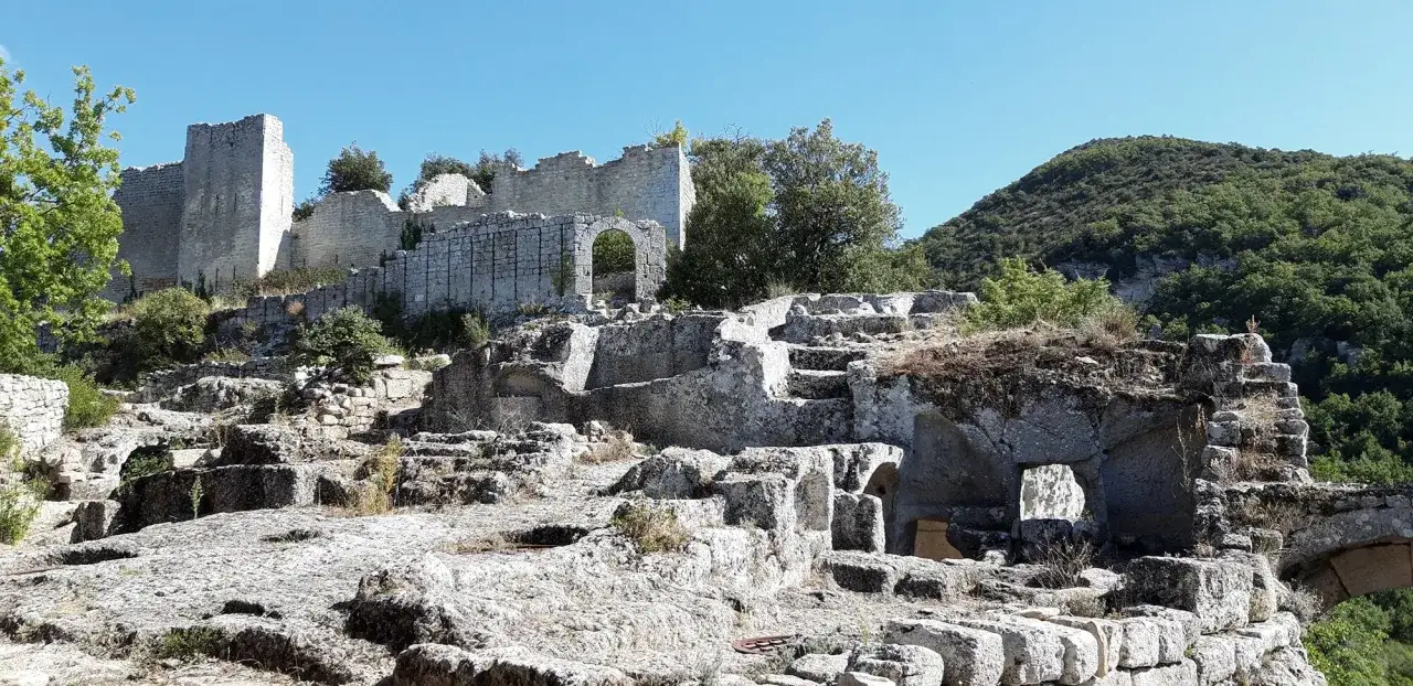 Ruines du fort de Buoux, un ch&acirc;teau m&eacute;di&eacute;val en pierre, avec des murs d&eacute;labr&eacute;s et des structures rocheuses sculpt&eacute;es, sous un ciel bleu clair.