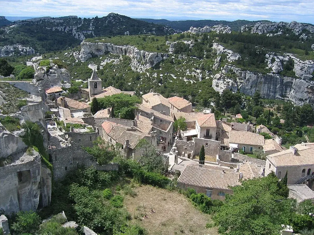 Vue aérienne du village perché des Baux-de-Provence, avec ses toits de tuiles ocres nichés dans un paysage rocheux et verdoyant.