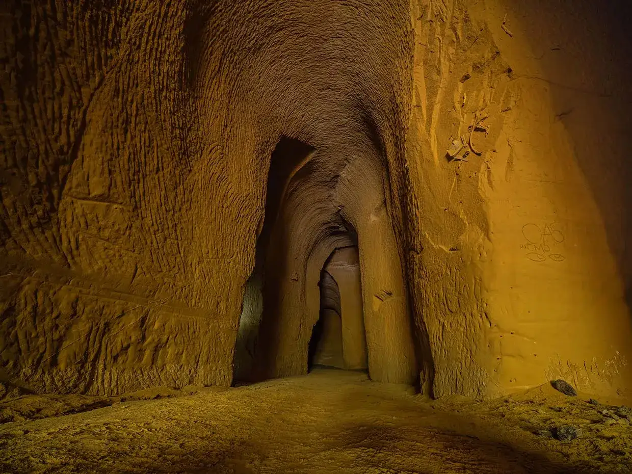 Int&eacute;rieur d'une carri&egrave;re d'ocre vaucluse aux parois sculpt&eacute;es, un tunnel sombre s'enfonce dans les profondeurs.