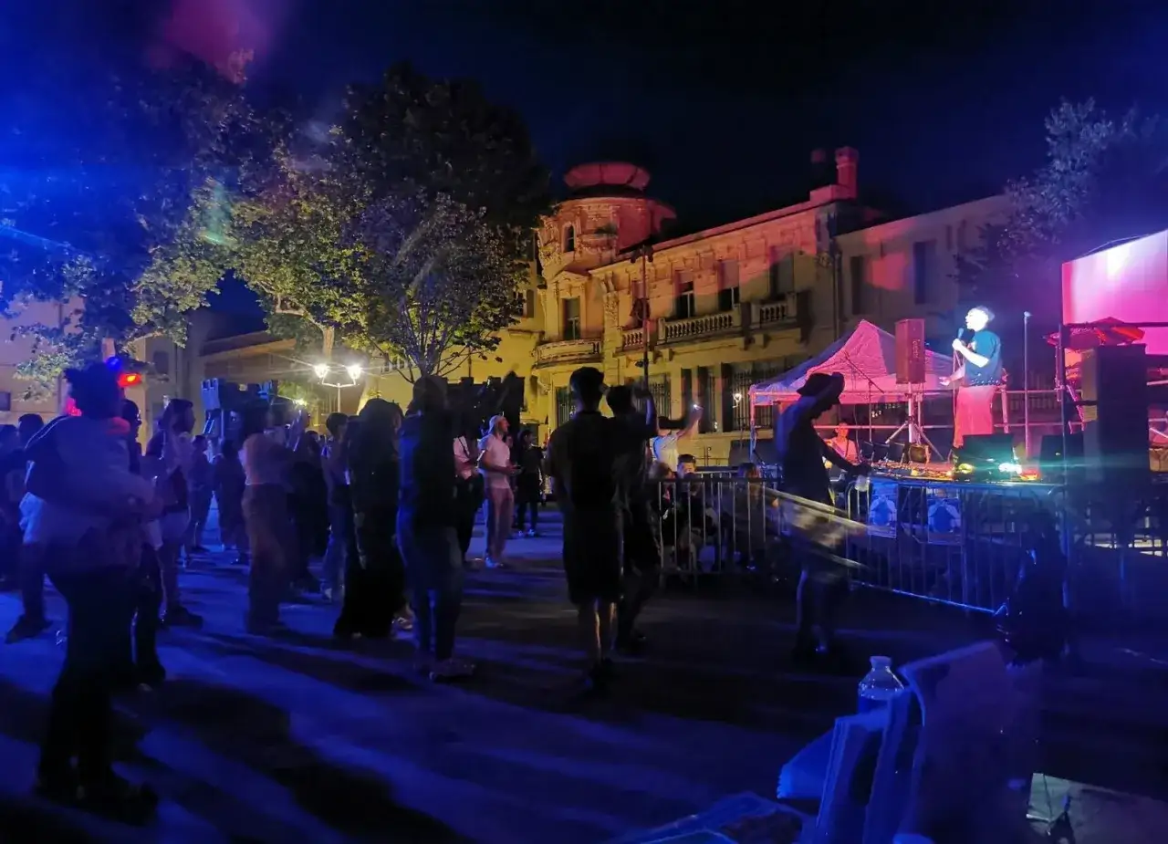 Une foule danse sous les lumi&egrave;res bleues et roses lors de la F&ecirc;te de la Musique &agrave; Carpentras. Un DJ mixe sur sc&egrave;ne, illumin&eacute; par les projecteurs.