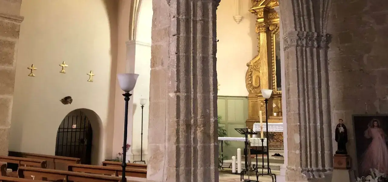 Int&eacute;rieur de l'&eacute;glise de Lourmarin, avec des bancs, un autel dor&eacute;, des lampes et des croix murales.
