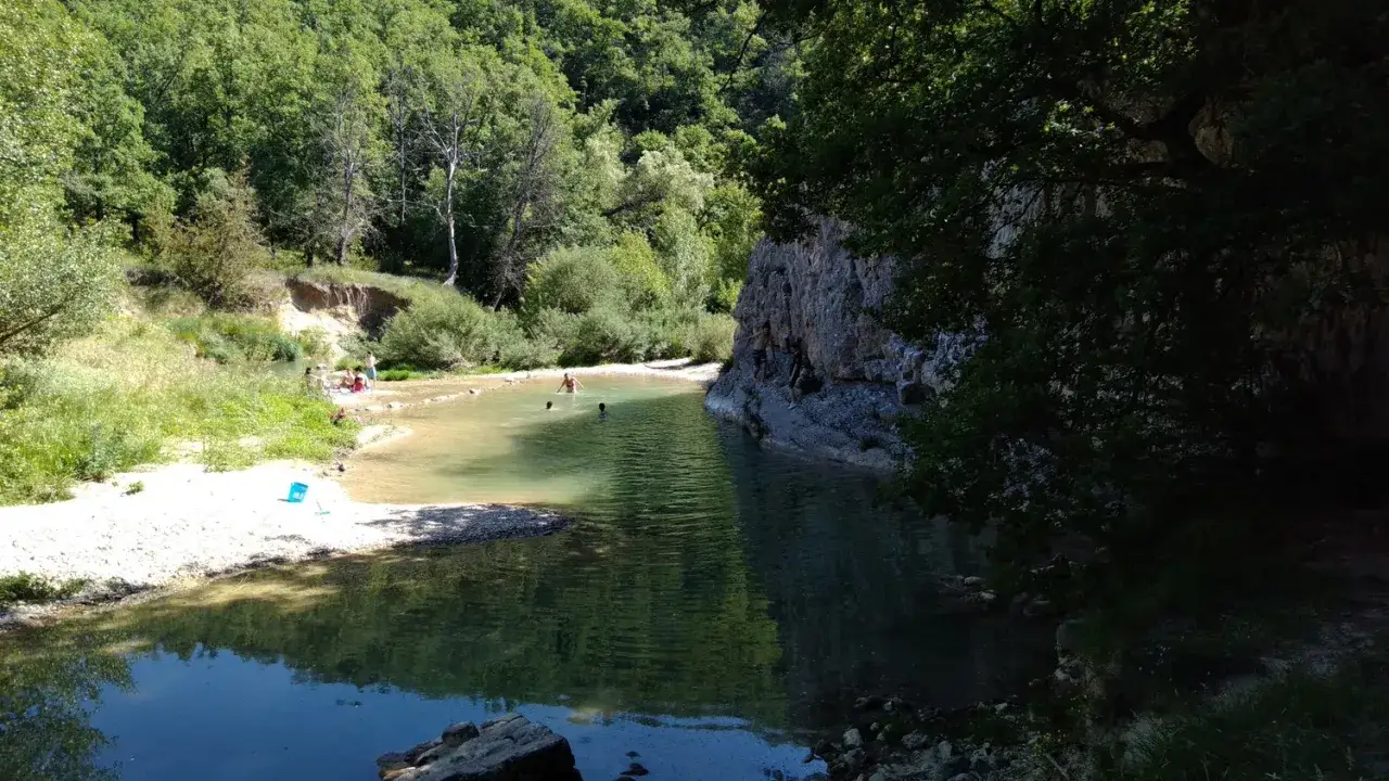 Des baigneurs profitent d'une rivière aux eaux claires près du rocher des abeilles, certains grimpent sur la paroi rocheuse.
