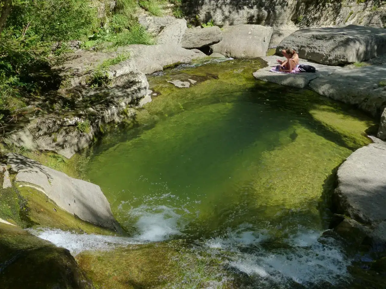 Une personne se repose au bord du lac du Bartras, une eau verte et limpide entour&eacute;e de rochers et de v&eacute;g&eacute;tation.