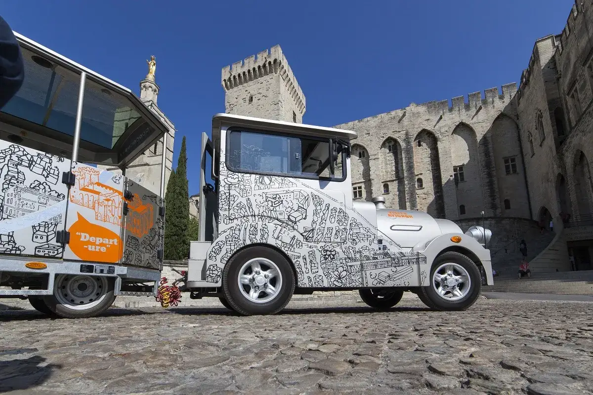Le petit train touristique d'Avignon, décoré de dessins de la ville, attend les visiteurs devant le Palais des Papes.