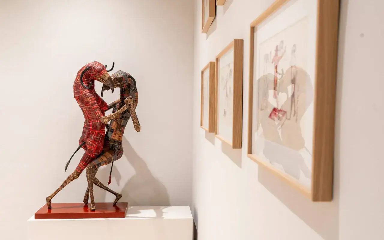 Sculpture de deux personnages en tissu &agrave; carreaux, expos&eacute;e &agrave; la fondation Blach&egrave;re, avec des dessins encadr&eacute;s sur le mur.