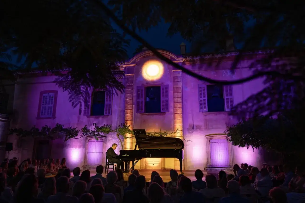 Un pianiste joue devant un public lors des nuits du ch&acirc;teau, le b&acirc;timent illumin&eacute; de lumi&egrave;res violettes et orang&eacute;es.
