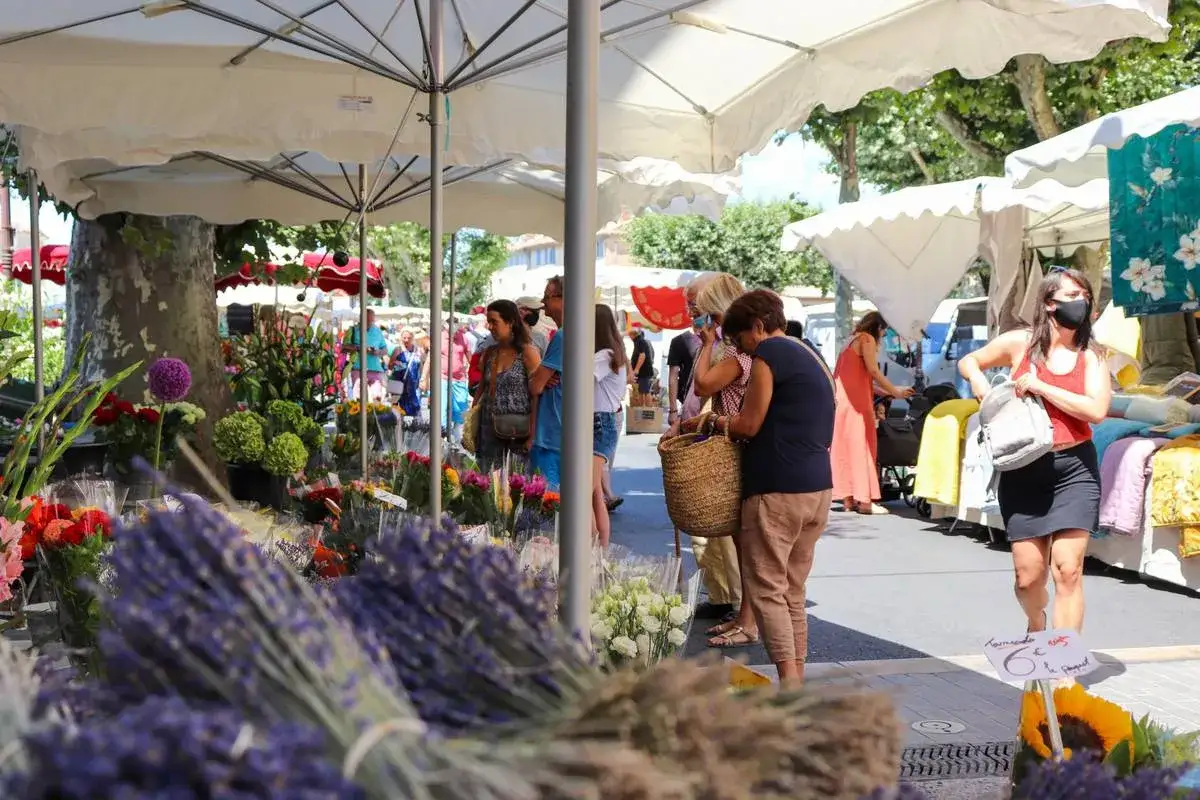 Ambiance anim&eacute;e au bonnieux markt, avec des &eacute;tals de fleurs color&eacute;es et des passants profitant du soleil.
