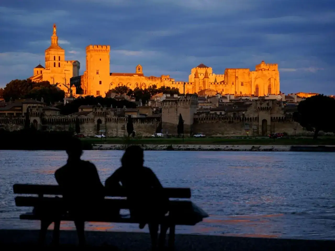 Couple admire le Palais des Papes au coucher du soleil, un moment parfait pour un guide Avignon.