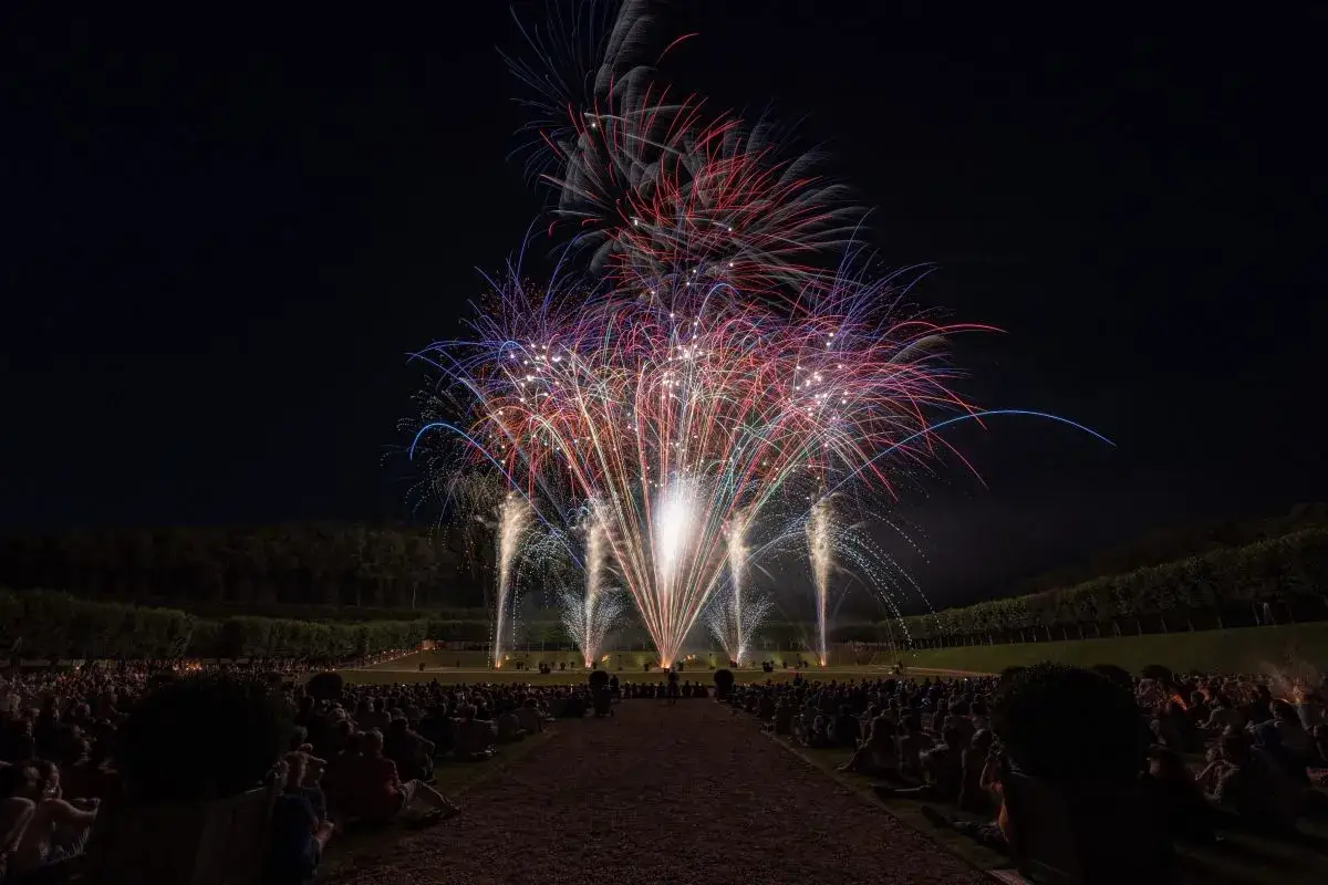 Spectacle de feu d'artifice &agrave; Lourmarin, illuminant le ciel nocturne de gerbes rouges, blanches et bleues au-dessus d'une foule admirative.