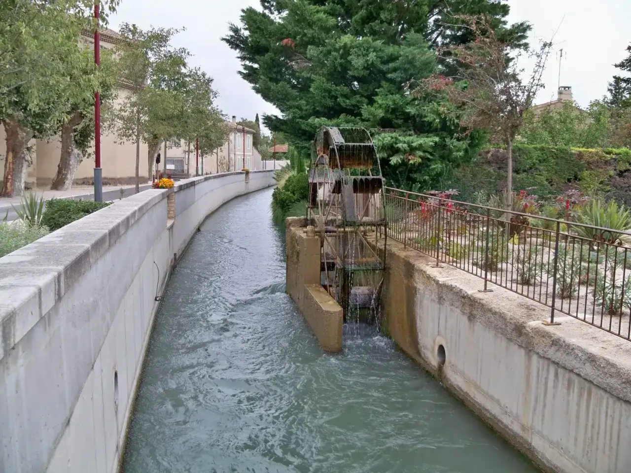 Un canal d'eau coule &agrave; travers un village du Vaucluse, une roue &agrave; aubes rouill&eacute;e tourne doucement.