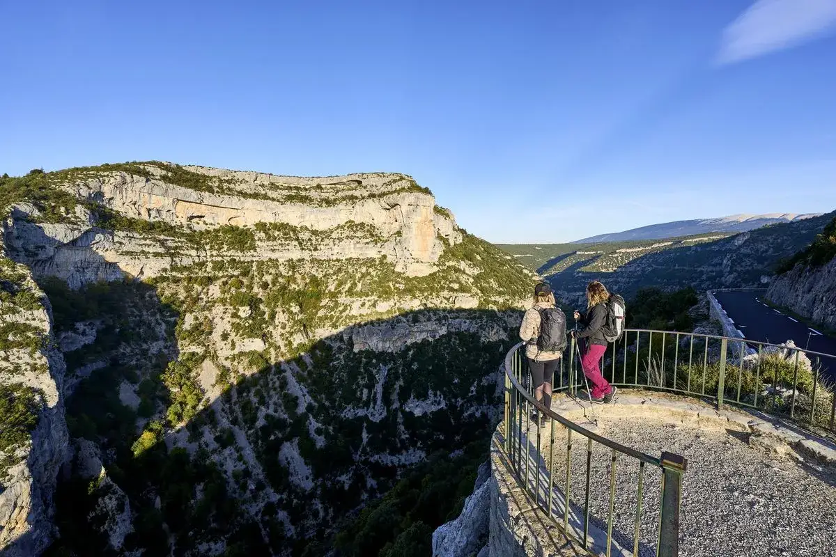 Deux randonneuses admirent le panorama spectaculaire des gorges de la Nesque. Le soleil illumine les falaises abruptes et la v&eacute;g&eacute;tation luxuriante.