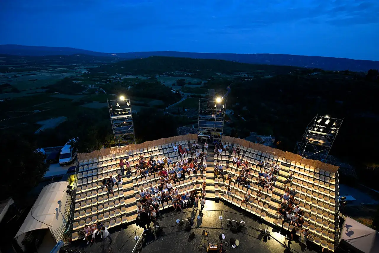 Amphith&eacute;&acirc;tre en plein air pour le festival de Gordes, avec un public assis attendant le spectacle sous un ciel bleu nuit.