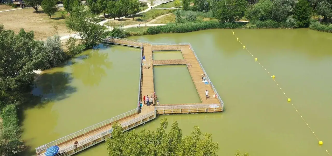 Pontons en bois sur un plan d'eau verd&acirc;tre, une base de loisirs &agrave; Apt. Des personnes profitent du soleil et de l'eau.