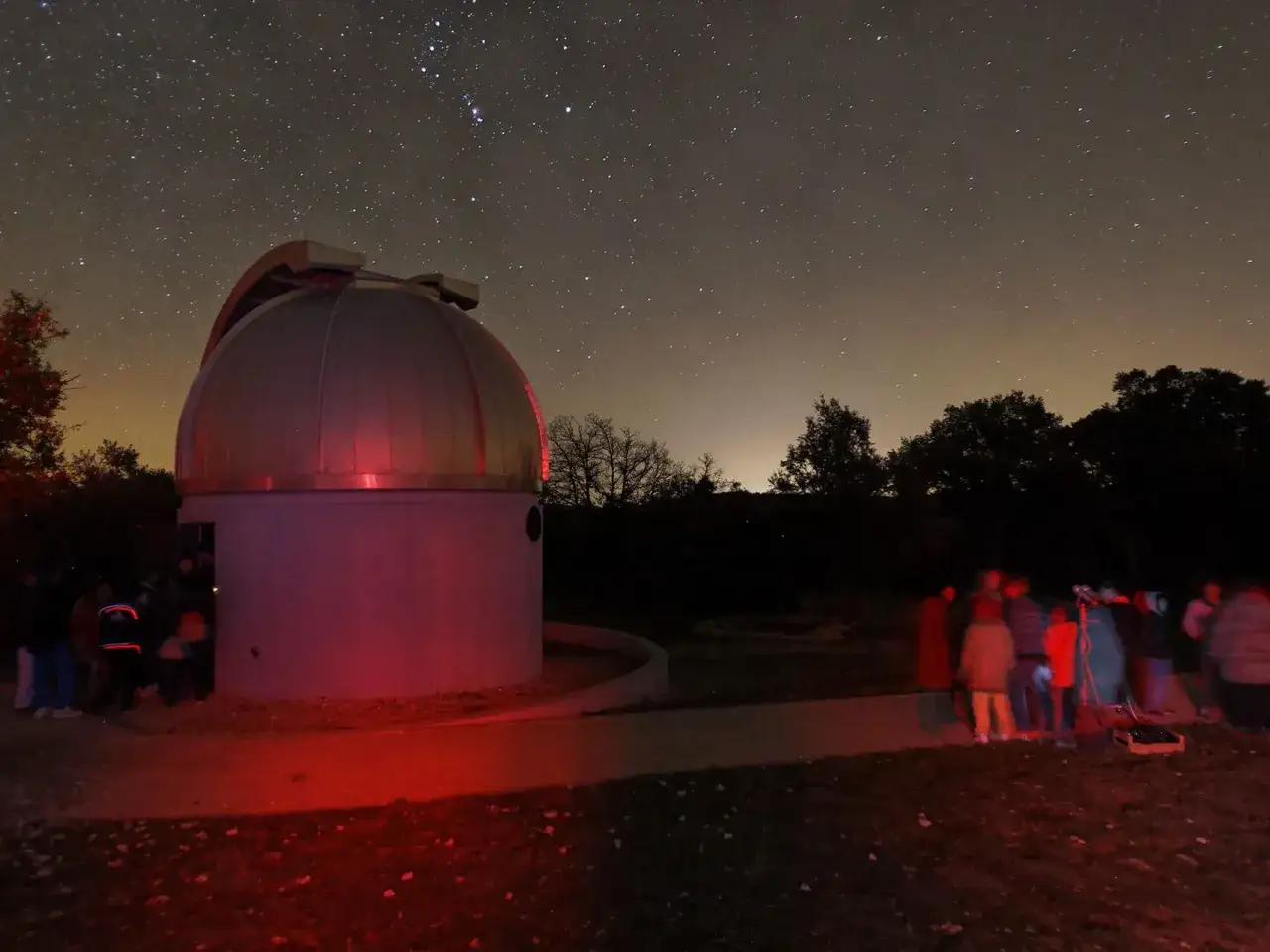 Nuit étoilée au saint michel l'observatoire. Un dôme d'astronomie baigné de lumière rouge, entouré d'une foule curieuse observant le ciel.